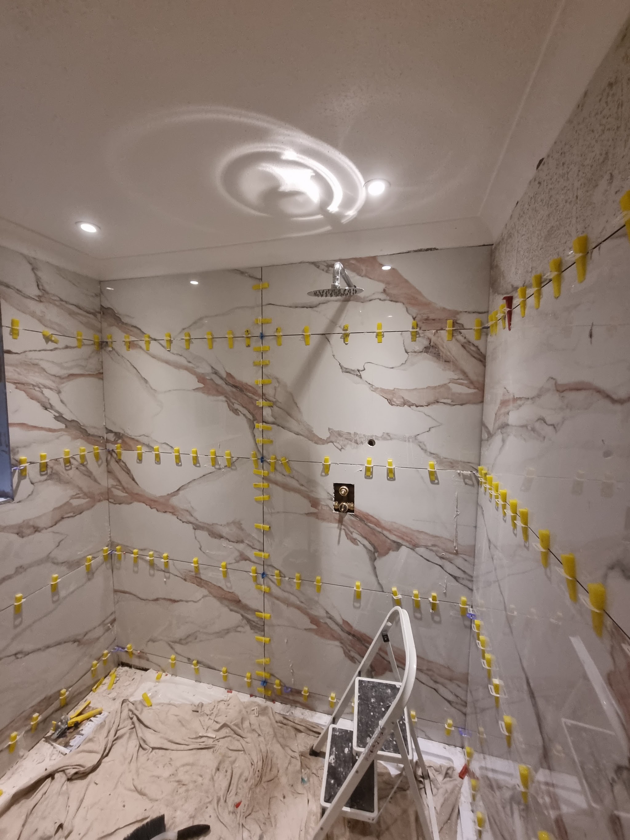 Marble-effect wall tiles going up in a shower area, with levelling clips in place