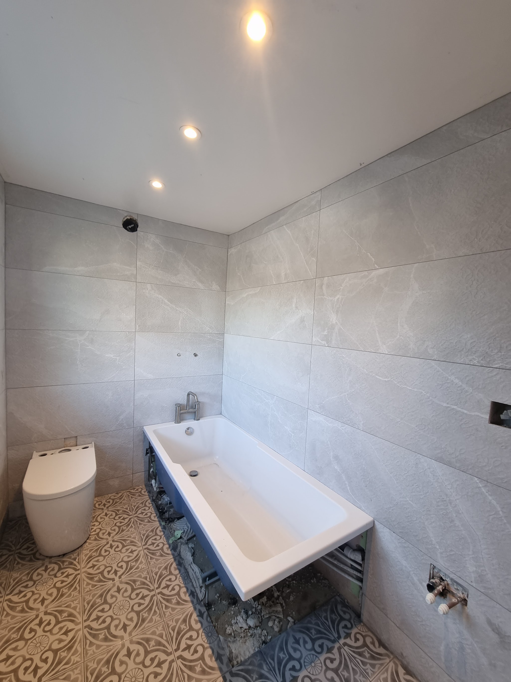Bathroom with large-format grey wall tiles and a patterned floor, part-way through the fit