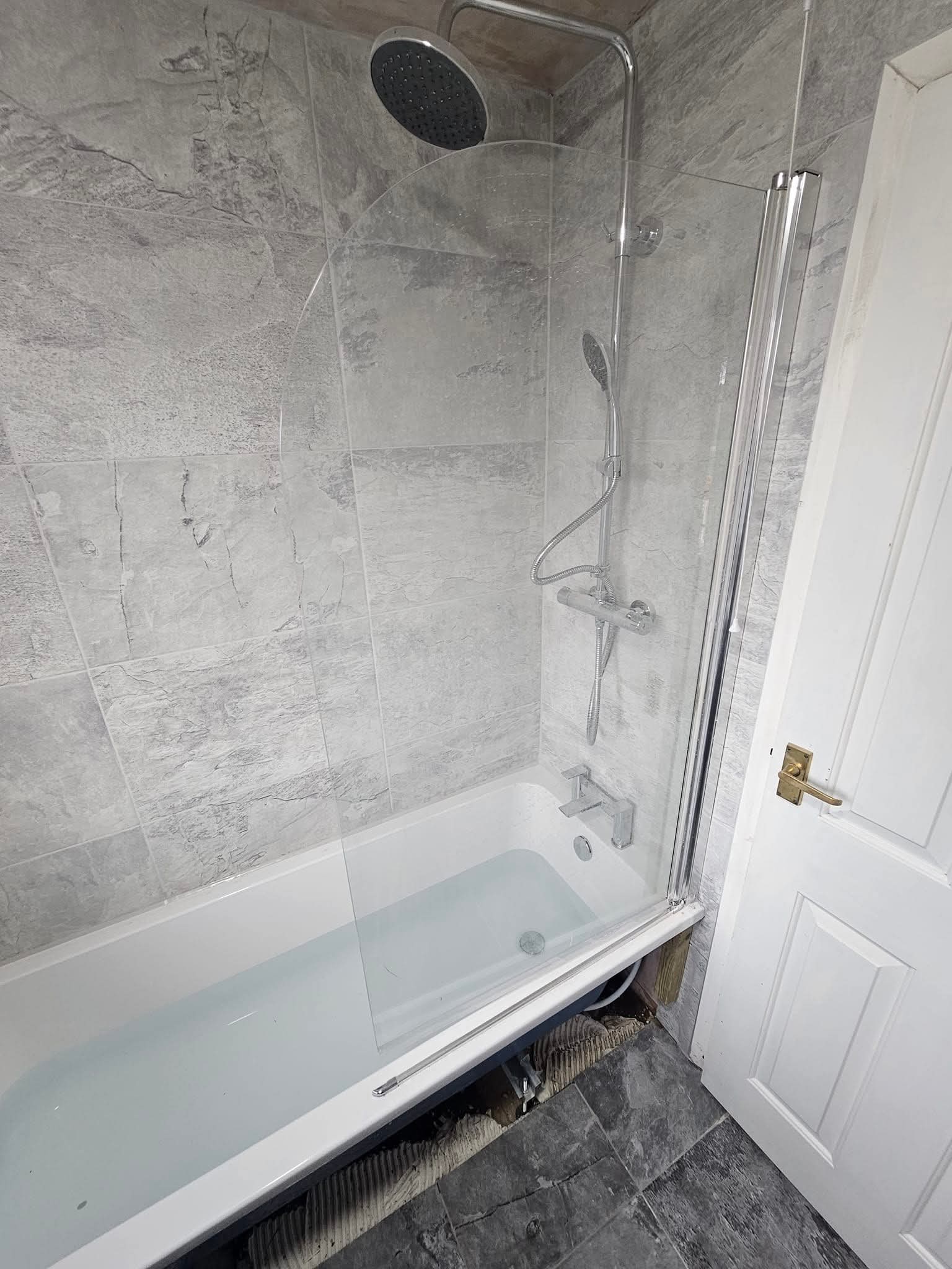 Finished bath with glass shower screen and grey marble-effect wall tiles